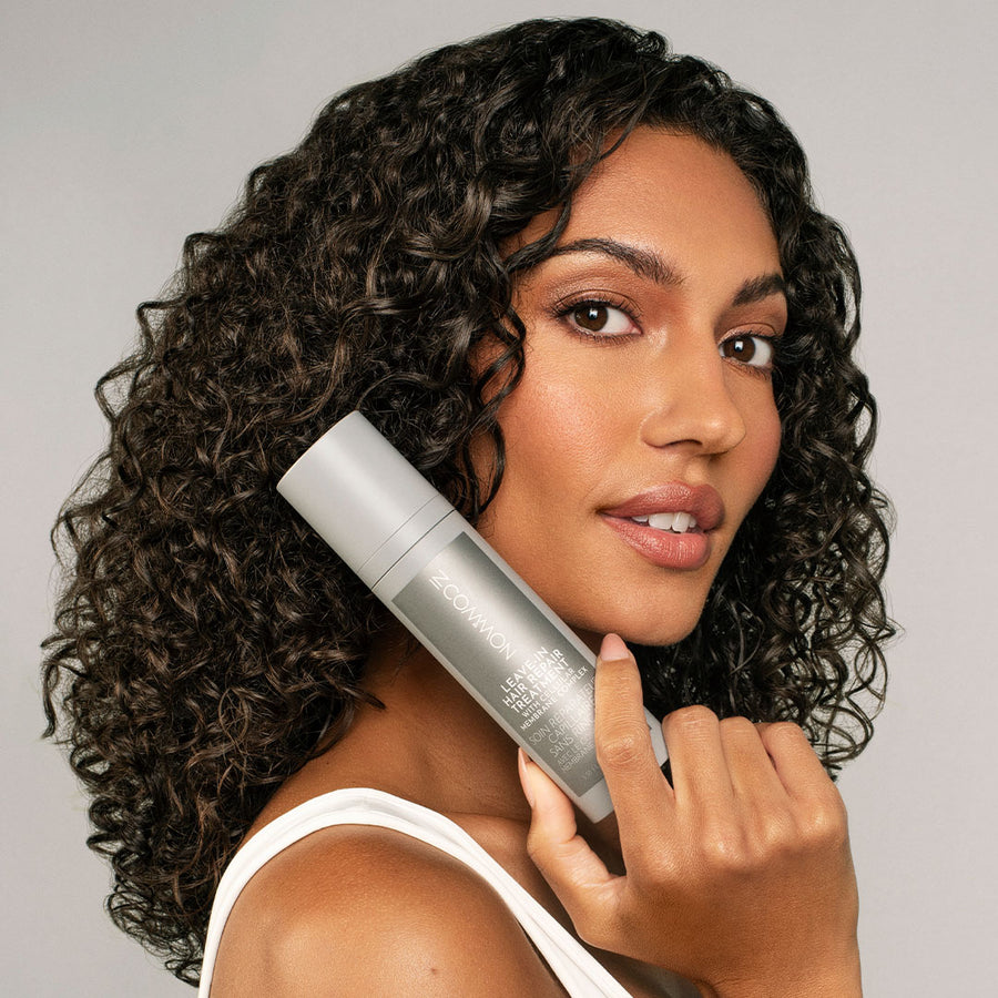 model with beautiful curly hair holding a bottle of Leave-In Hair Repair Treatment with Cellular Membrane Complex next to her face